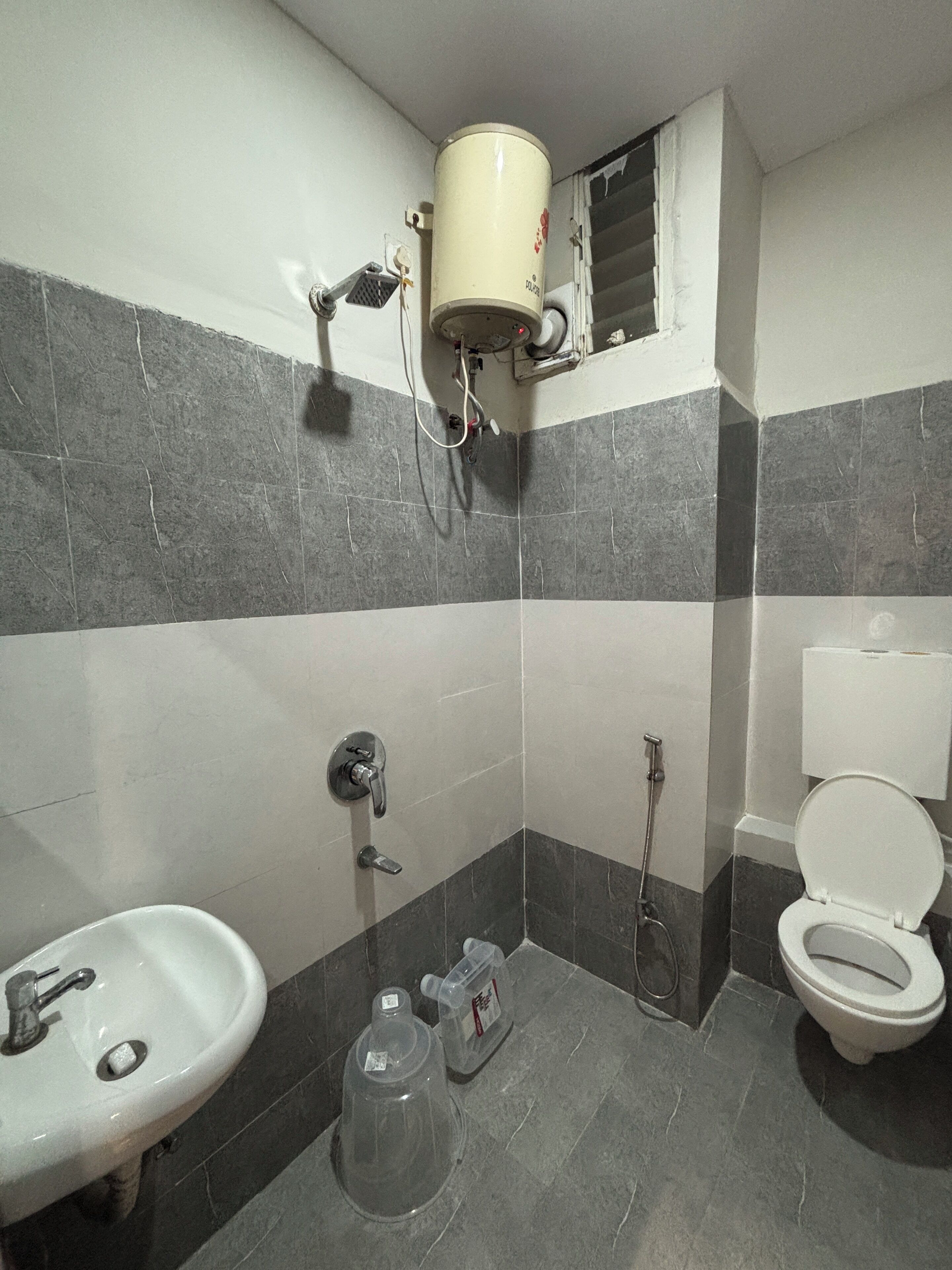 A bathroom with a toilet, sink, shower, and a water heater mounted on the wall.