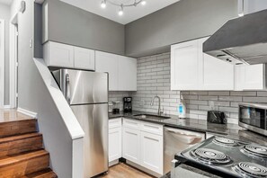 Una cocina moderna con armarios blancos, un refrigerador de acero inoxidable, una estufa a gas y un microondas.