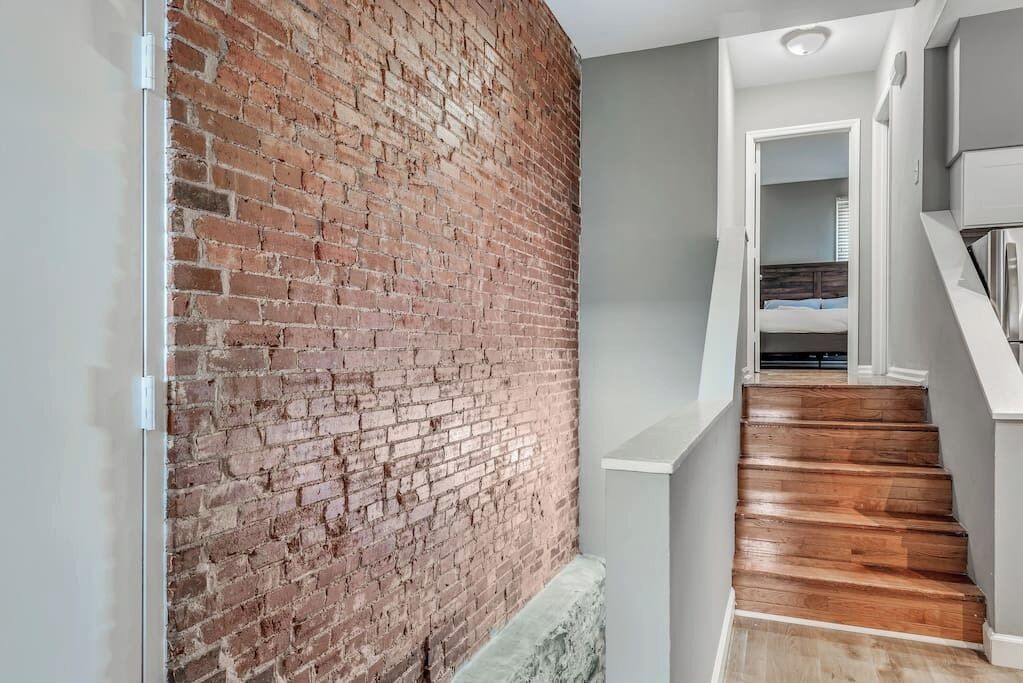 A staircase with wooden steps leading to a bedroom with a bed and a nightstand.