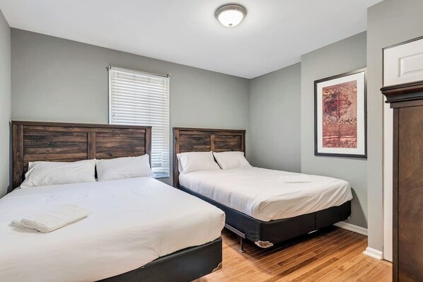 Habitación de hotel con dos camas, una ventana con persianas, una obra de arte enmarcada en la pared y piso de madera.