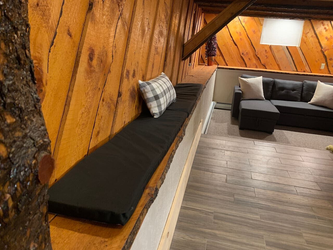 Een knus zolderkamertje met een houten schuine plafond, een zwarte bank met ruitkussen, en een donkergroene bank met witte kussens.