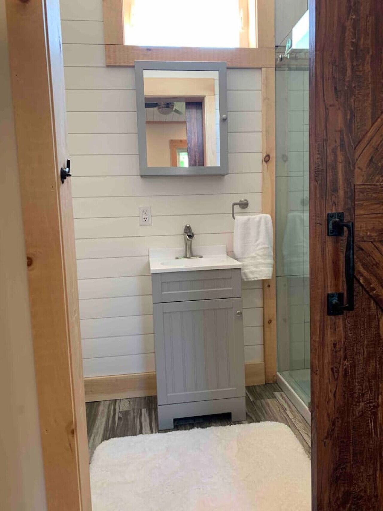 A bathroom with a wooden door, a white sink, a mirror, and a shower area.