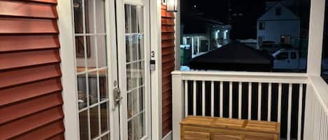 Une terrasse en bois avec une balustrade blanche, un banc et une porte à panneaux de verre.