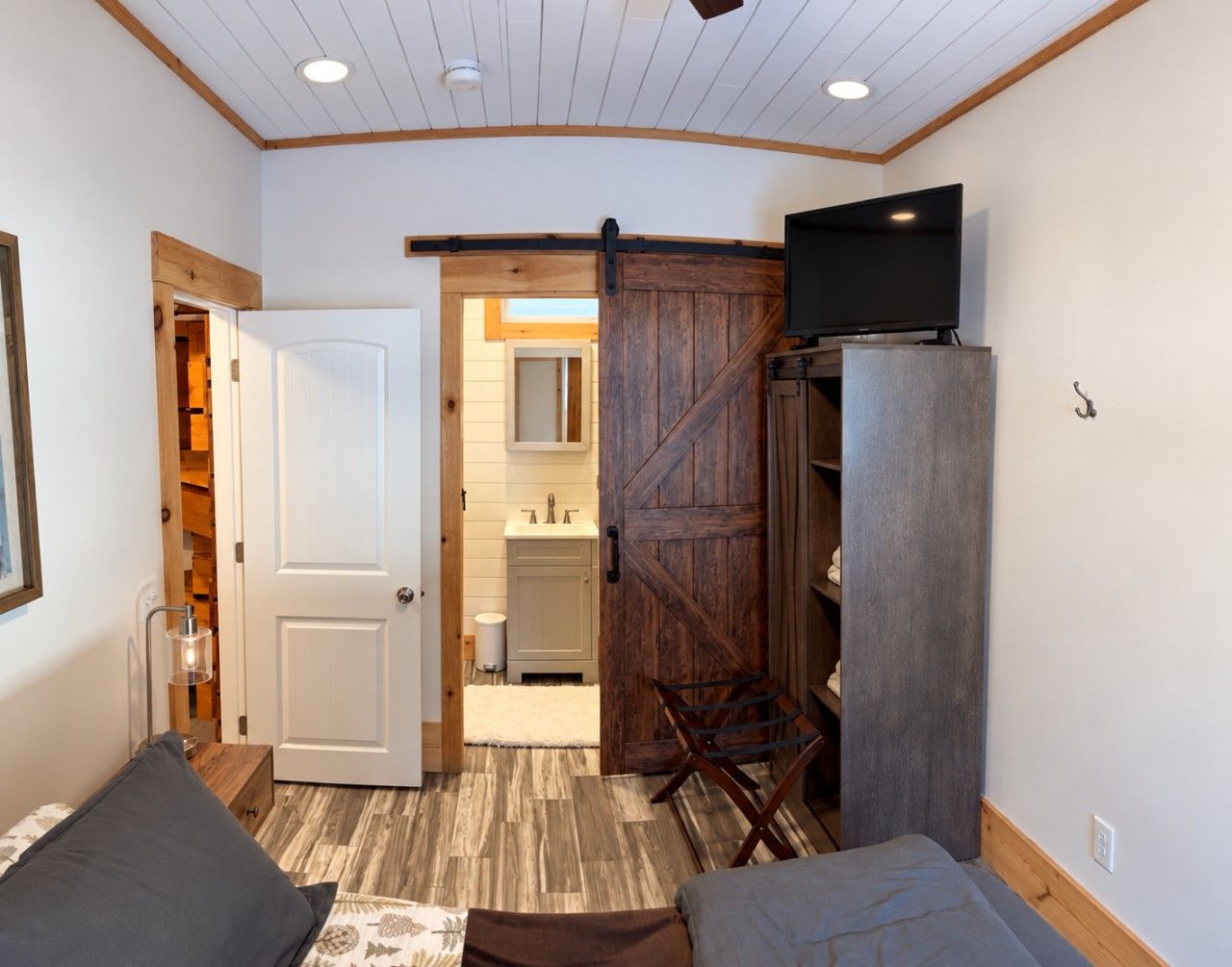 A room with a bed, a television on a stand, a wooden door, and a wardrobe.