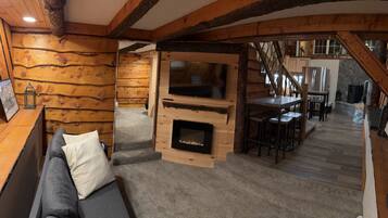 A cozy log cabin interior with a fireplace, a sofa, and a dining area.