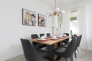 A dining area with a wooden table, six chairs, and a chandelier. There are two framed artworks on the wall. - Chic 4BR Home Storey Lake - Near Disney (Kissimmee)