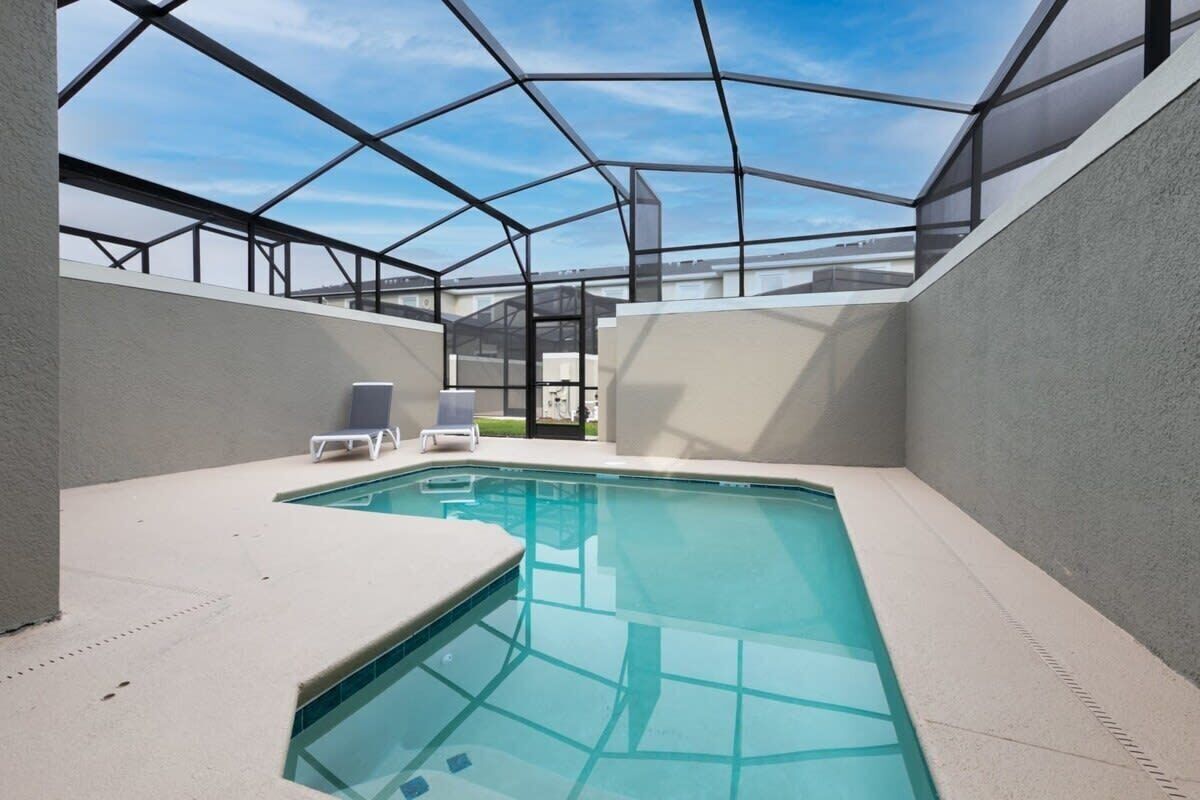 A modern indoor swimming pool with a glass ceiling, surrounded by walls and a poolside area with lounge chairs.