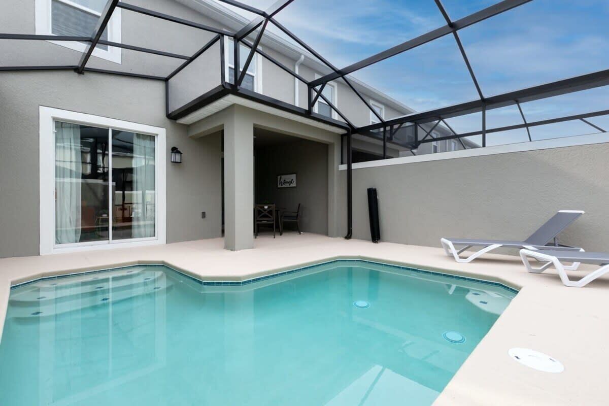 A modern outdoor pool area with a glass ceiling, a lounge chair, and a small seating area.