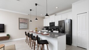 A modern kitchen with white cabinets, a stainless steel refrigerator, a microwave, and a large island with bar stools. - Chic 4BR Home Storey Lake - Near Disney (Kissimmee)