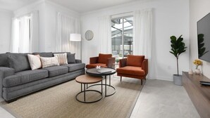 A modern living room with a grey sofa, two armchairs, a coffee table, and a large window with curtains. - Chic 4BR Home Storey Lake - Near Disney (Kissimmee)