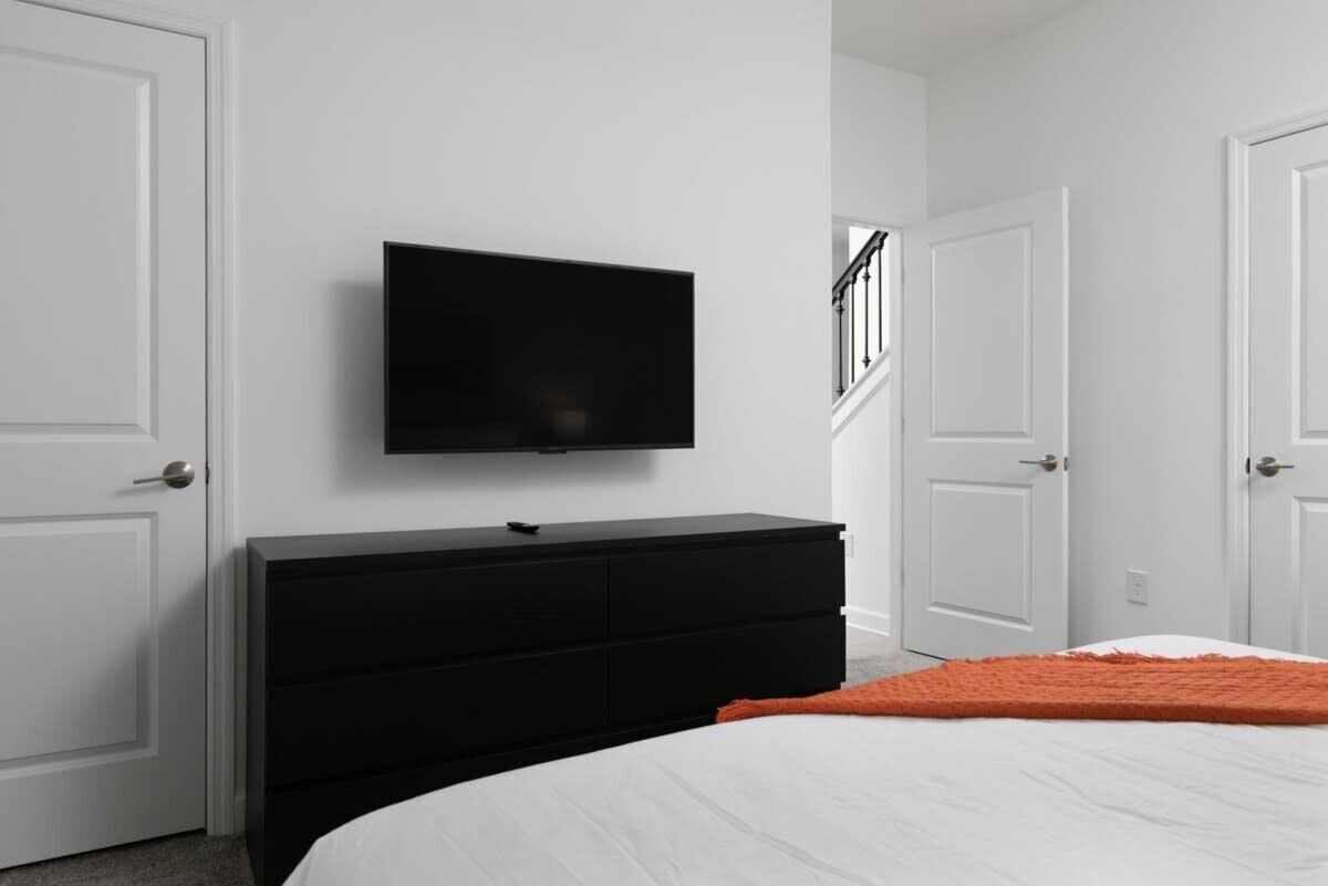 A bedroom with a black dresser, a flat-screen TV mounted on the wall, and white doors.