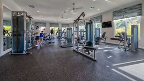 A modern gym with various exercise machines, large windows, and a ceiling fan. - Storey Lake 4BR Townhome - 10 min to Disney (Kissimmee)