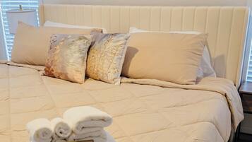 A neatly made bed with a beige comforter and pillows, a sign with fresh towels, and a large abstract painting on the wall.