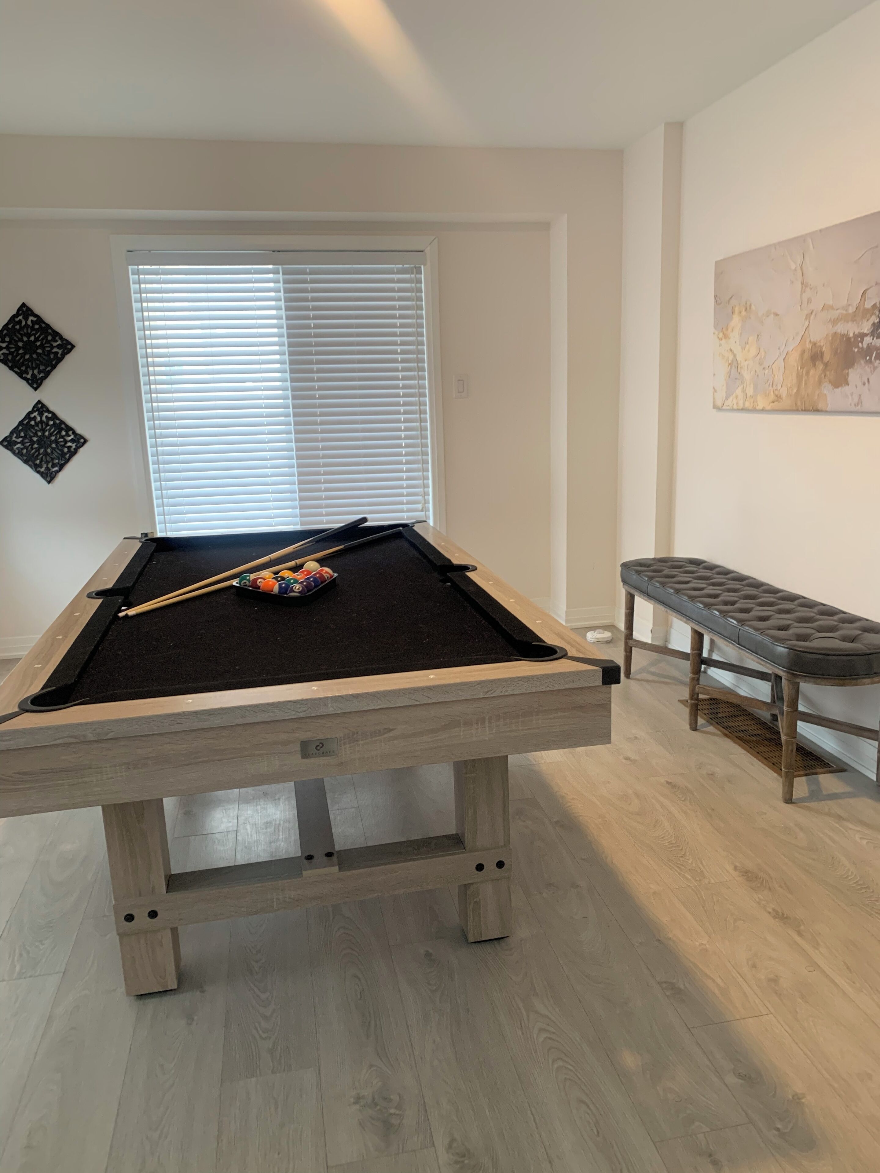 A pool table with a black felt surface, surrounded by light-colored wooden flooring.