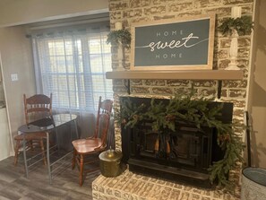 A cozy living room with a fireplace, a dining table with chairs, and a sign above the fireplace that reads "HOME sweet HOME". - New - Crestwood Peak. Spacious - 2200sf-  3-bedroom house in Central Kilgore. (Kilgore)