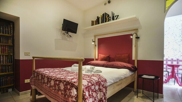 A bedroom with a four-poster bed, a television mounted on the wall, and a bookshelf filled with books. - RIPA HOME LOFT IN TRASTEVERE (Roma)