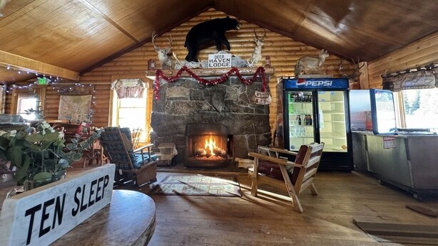 Interior acogedor de una cabaña con chimenea de piedra, techo de madera y un cartel que dice 'Ten Sleep'.