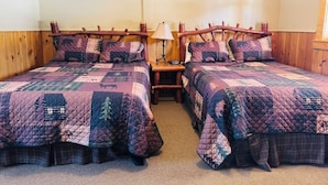Una habitación con dos camas de madera, cada una con cubrecama acolchado y almohadas a juego. Hay una mesita de noche con una lámpara entre las camas.