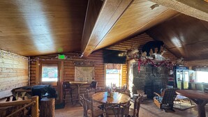 Un interior rústico de madera con una mesa redonda para comer rodeada de sillas, una chimenea de piedra y un techo de madera.