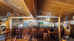 Un rústico espacio de bar con mobiliario de madera, una barra y diversas botellas de licores.