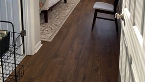 Quarto com cama, uma cadeira, ventoinha no teto e duas janelas com persianas.
