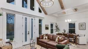 A spacious living room with a brown leather sofa, green armchairs, a wooden coffee table, and a dining area with a white chair and table. - New! 4 BDRM Home near stockyards & DT Fort Worth (Fort Worth)