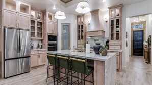 A modern kitchen with wooden cabinets, a stainless steel refrigerator, a marble island with bar stools, and pendant lighting. - New! 4 BDRM Home near stockyards & DT Fort Worth (Fort Worth)