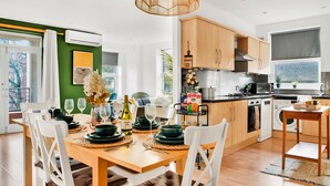 A modern kitchen with wooden cabinets, a dining area with a table set for four, and a view of the outside through a large window. - Spacious NG1 City Centre Apartment Near Motorpoint Arena, sleeps 6 (Nottingham)