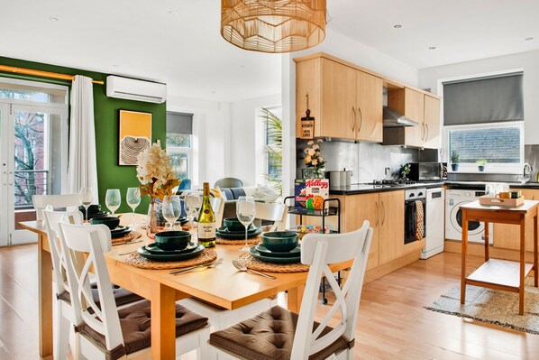 A modern kitchen with wooden cabinets, a dining area with a table set for four, and a view of the outside through a large window.