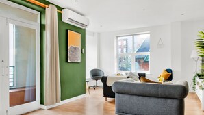 A modern living room with a grey sofa, a dining table with chairs, a large window, and an air conditioning unit on the wall. - Spacious NG1 City Centre Apartment Near Motorpoint Arena, sleeps 6 (Nottingham)