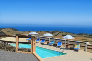 A pool area with blue lounge chairs and umbrellas, overlooking a coastal landscape. - appartamento 3 postil letto con angolo cottura (Palmadula)