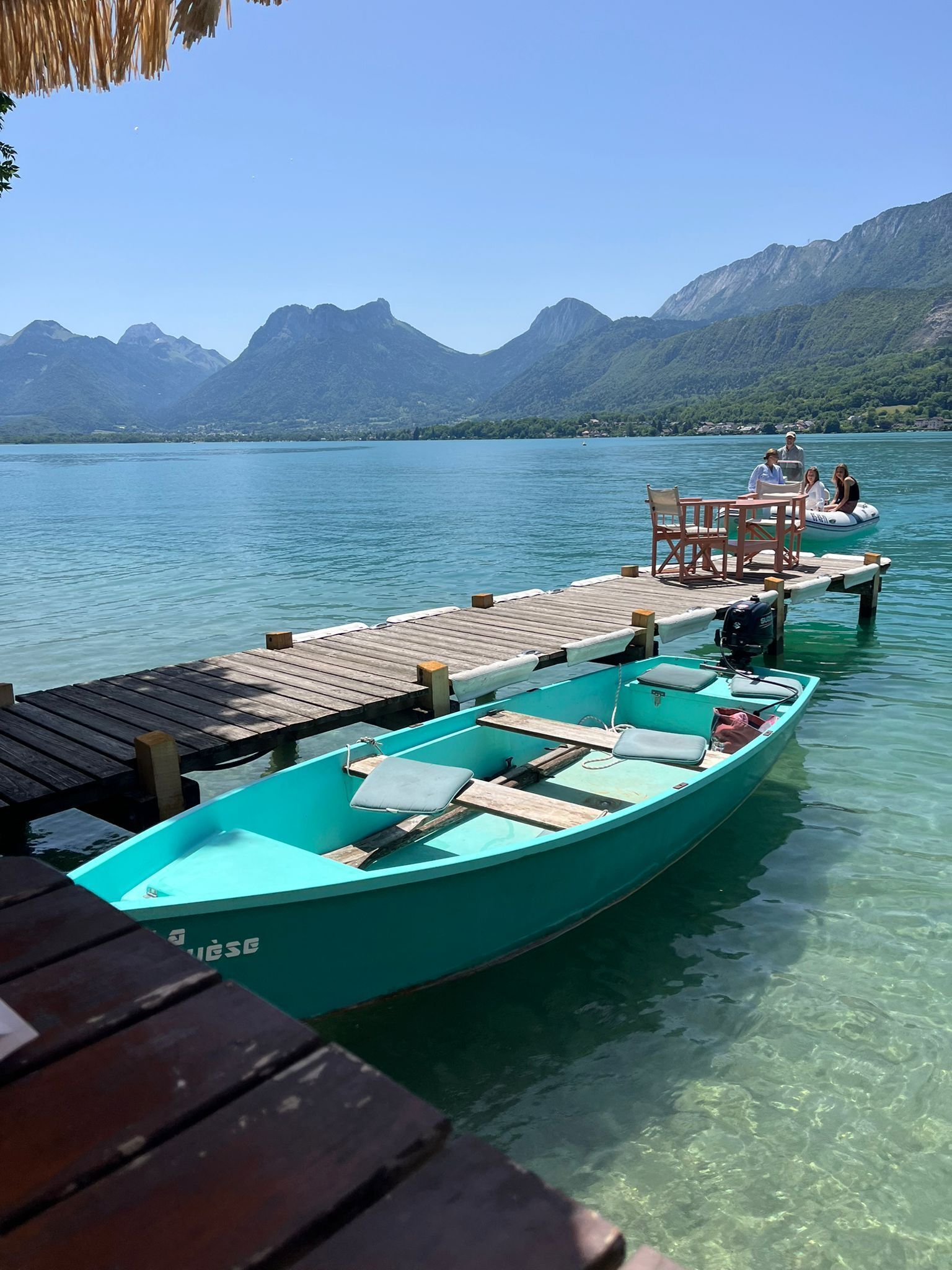 Un bateau turquoise était amarré à un quai en bois, d’où l’on pouvait admirer une vue dégagée sur les montagnes en arrière-plan.