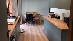 A compact kitchen with wooden countertops, a dining area with a table and chairs, and a visible fire extinguisher. - Wonderful modern Chalet with private garden only 5 minutes walk to Annecy Lake. (Doussard)