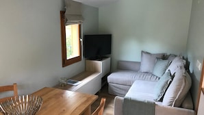 A compact living space with a wooden dining table, a sofa, and a television. - Wonderful modern Chalet with private garden only 5 minutes walk to Annecy Lake. (Doussard)
