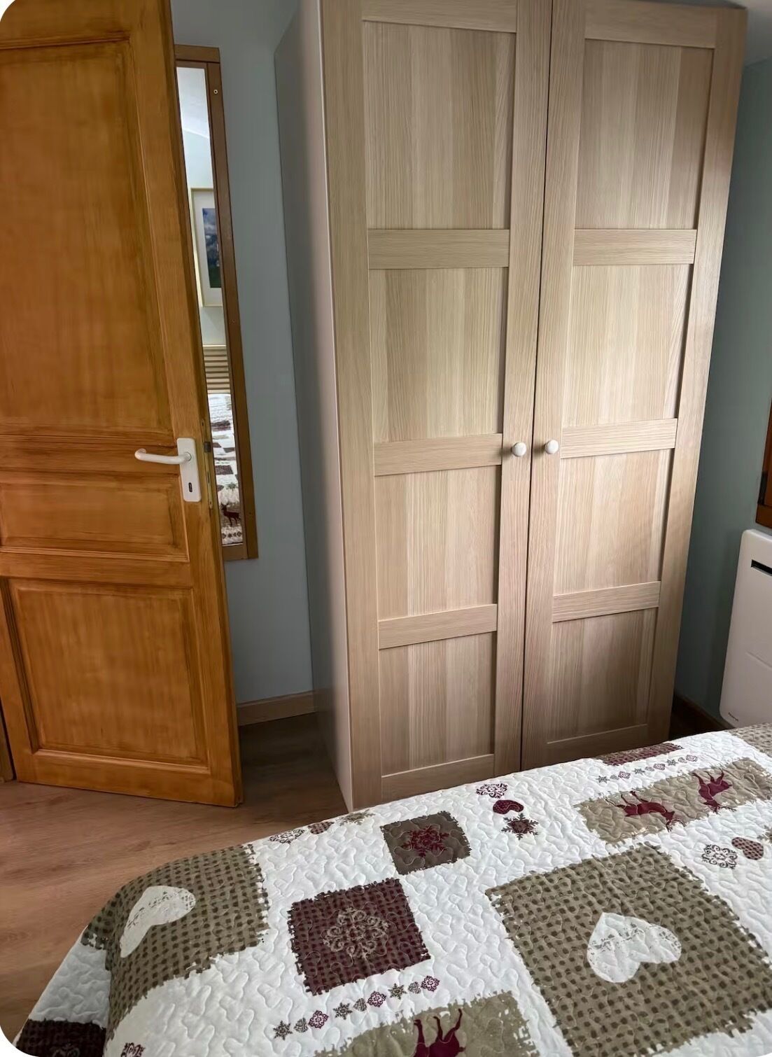 Ein Schlafzimmer mit einem Holzschrank, einem Bett mit Steppdecke und einem weißen Nachttisch.