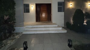 A modern entrance with a wooden door, steps, and two wall-mounted lights. - Luxury 5-Bedroom Hotel Villa – Palm Valley Compound, Sheikh Zayed, Egypt (El Sheikh Zayed City)