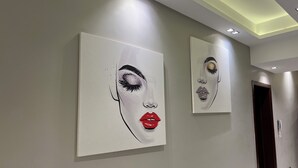 A hallway with two large wall-mounted artworks depicting abstract faces, a modern light fixture on the ceiling, and a door at the end. - Luxury 5-Bedroom Hotel Villa – Palm Valley Compound, Sheikh Zayed, Egypt (El Sheikh Zayed City)