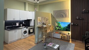 Eine moderne Küche mit weißen Schränken, einem Einbauofen und einer Waschmaschine. Ein Essbereich mit Tisch und Stühlen lädt zum Verweilen ein, und ein großes Fenster bietet Blick ins Grüne.