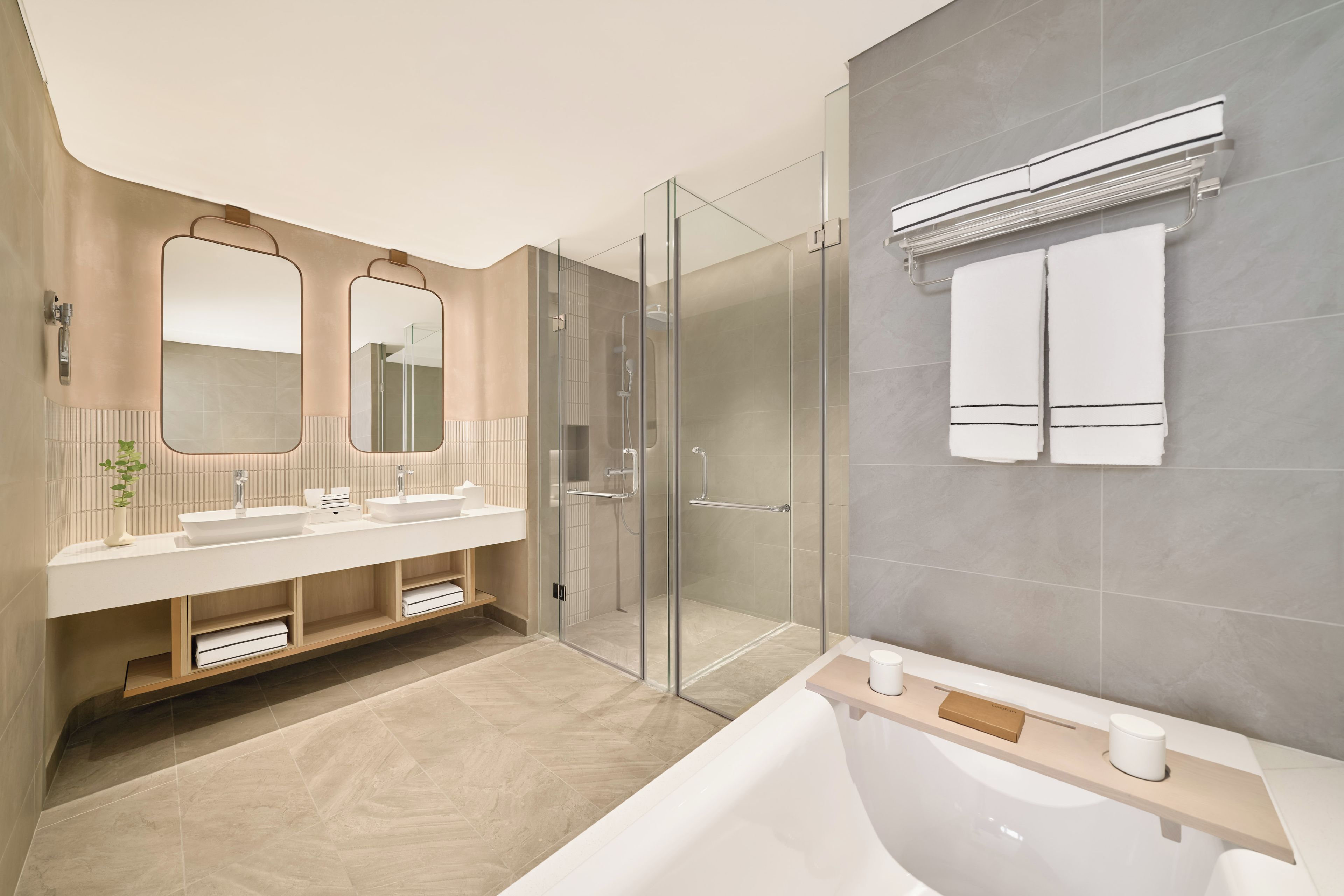 A modern bathroom with a glass-enclosed shower, a large bathtub, and a vanity with two sinks.