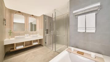 A modern bathroom with a glass-enclosed shower, a large bathtub, and a vanity with two sinks.