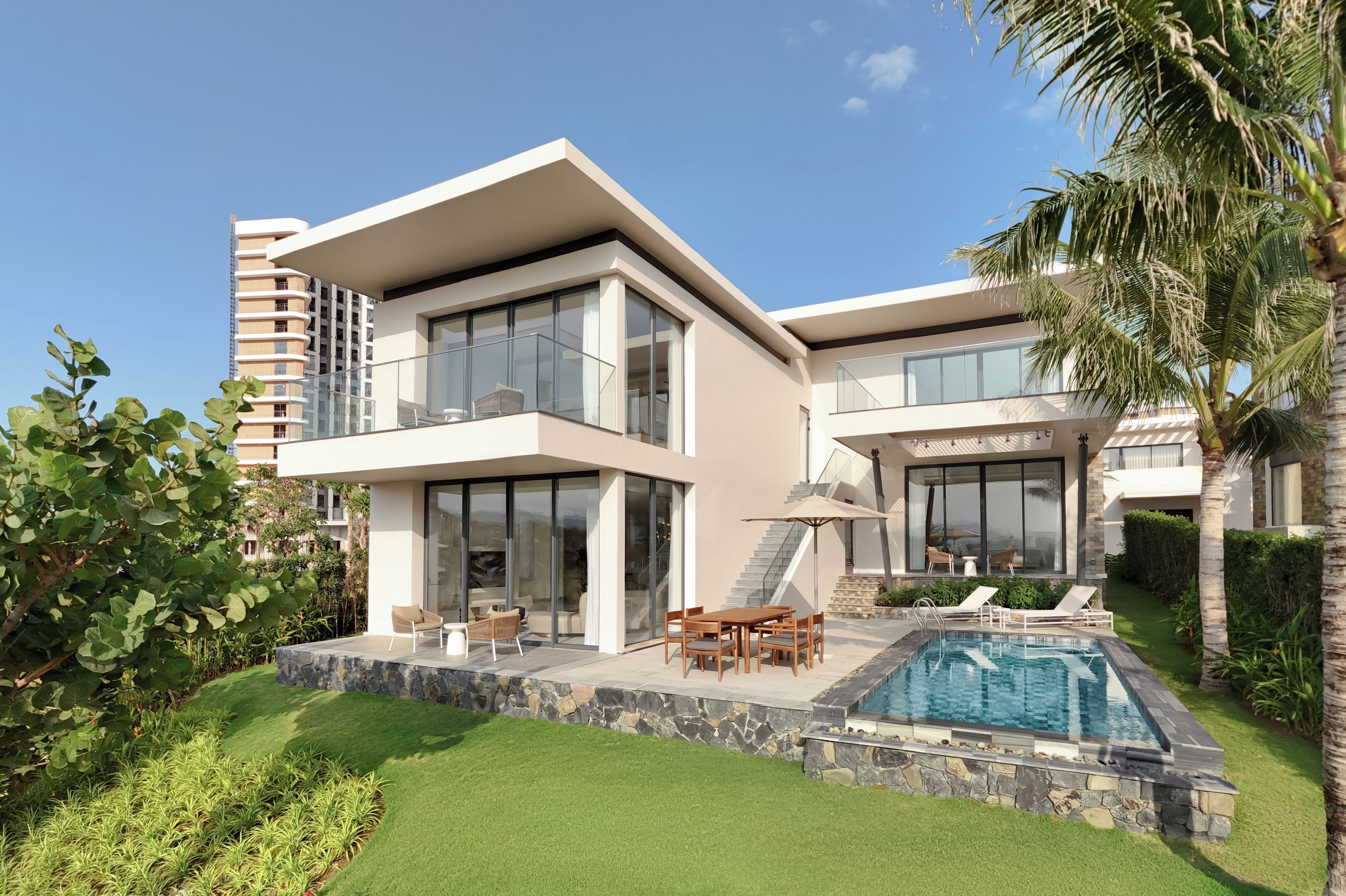 A modern two-story house with a swimming pool, outdoor seating, and lush greenery.