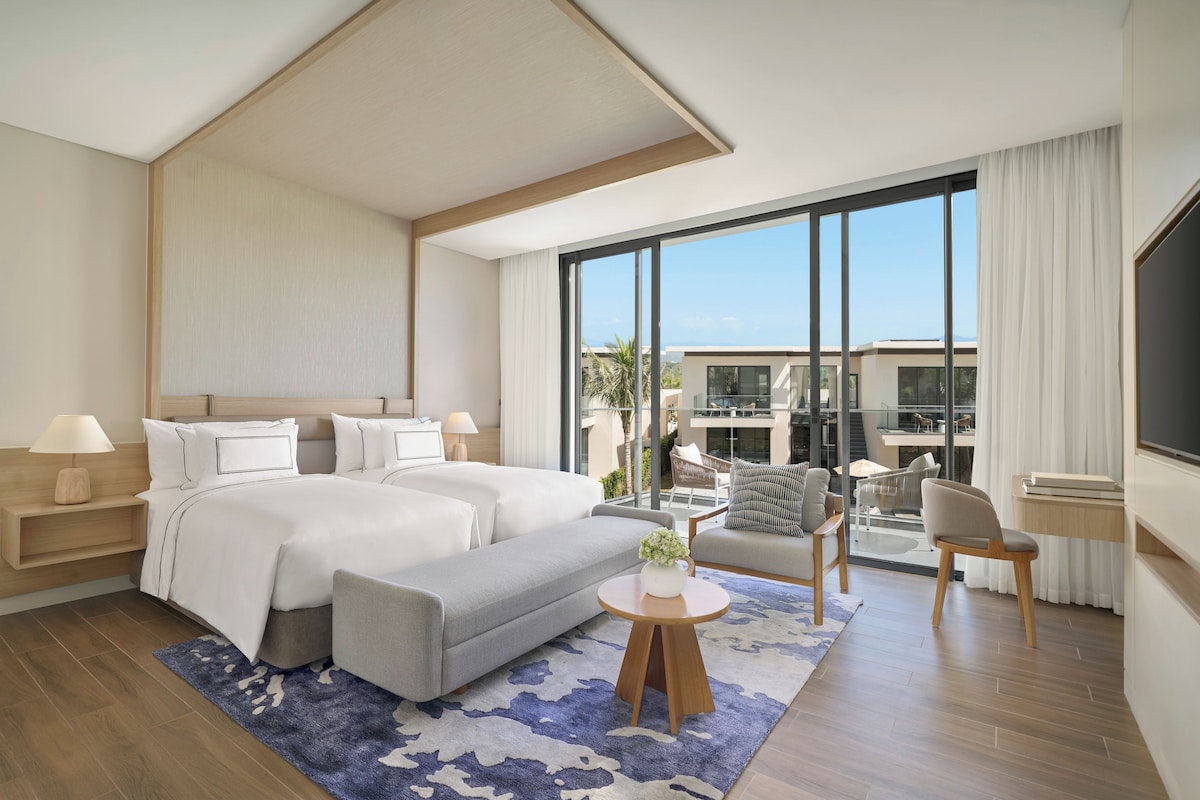 Una habitación de hotel moderna con una cama grande, una zona de estar y vistas a la ciudad.