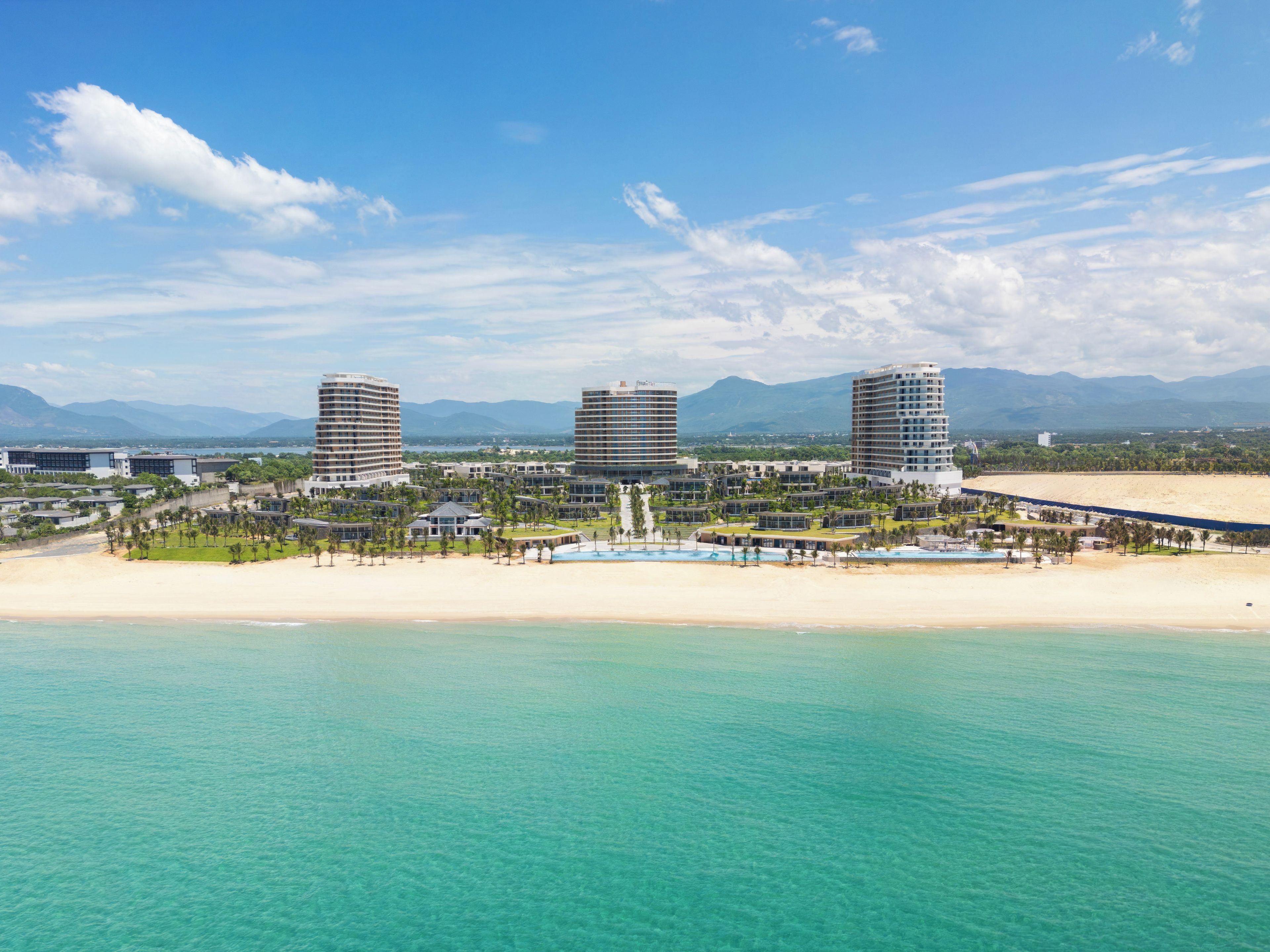 Un complejo turístico costero con varios edificios de gran altura, una playa de arena y aguas turquesas cristalinas.