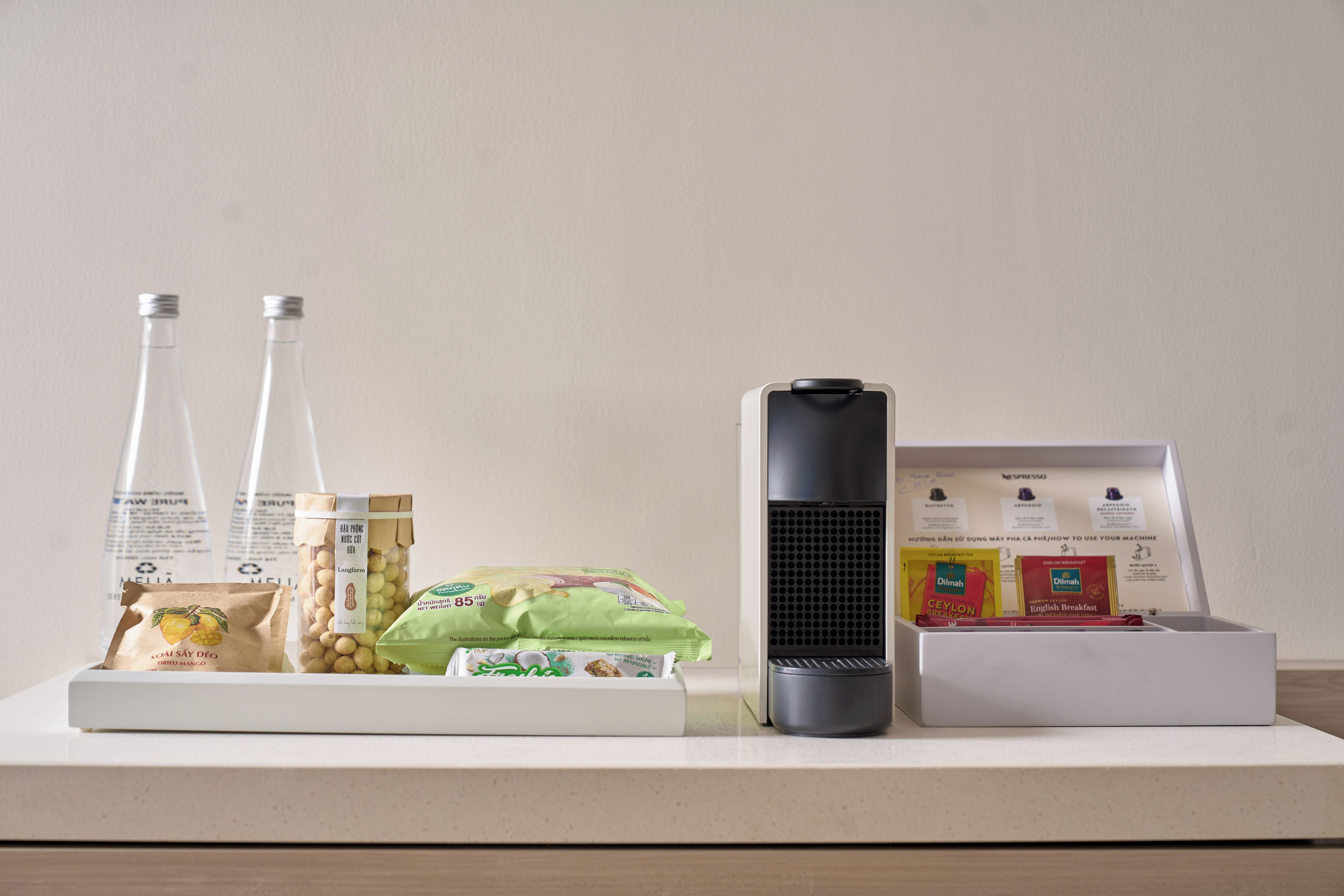 A kitchen counter with a coffee maker, a bottle of water, a bag of dried mango, a packet of tea, and a box of instant coffee.