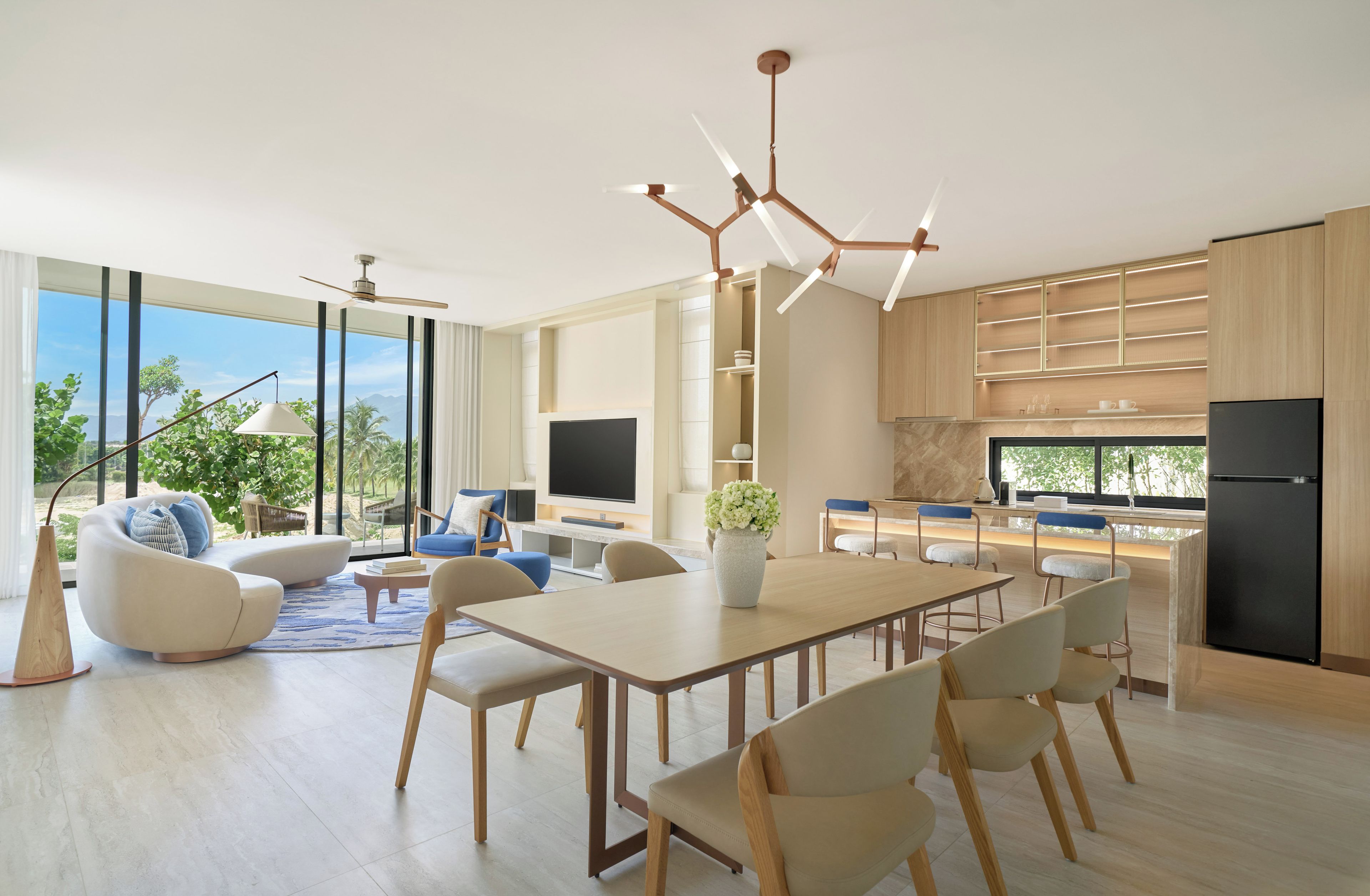 A modern kitchen with a dining area, large windows, and a view of greenery.
