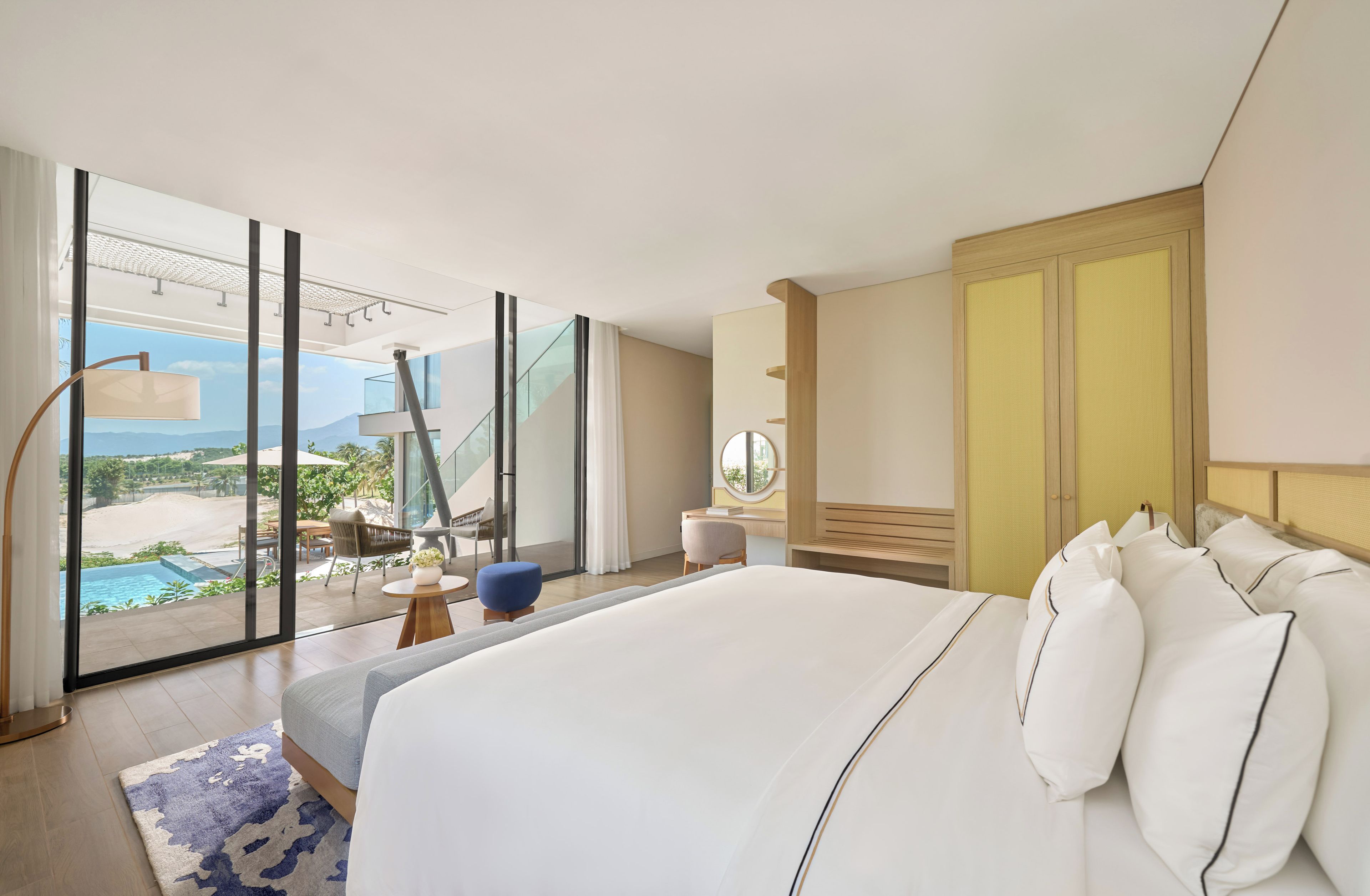 Une chambre d’hôtel moderne dotée d’un grand lit, offrant une vue sur une piscine et un espace extérieur, et munie d’une porte-fenêtre coulissante.