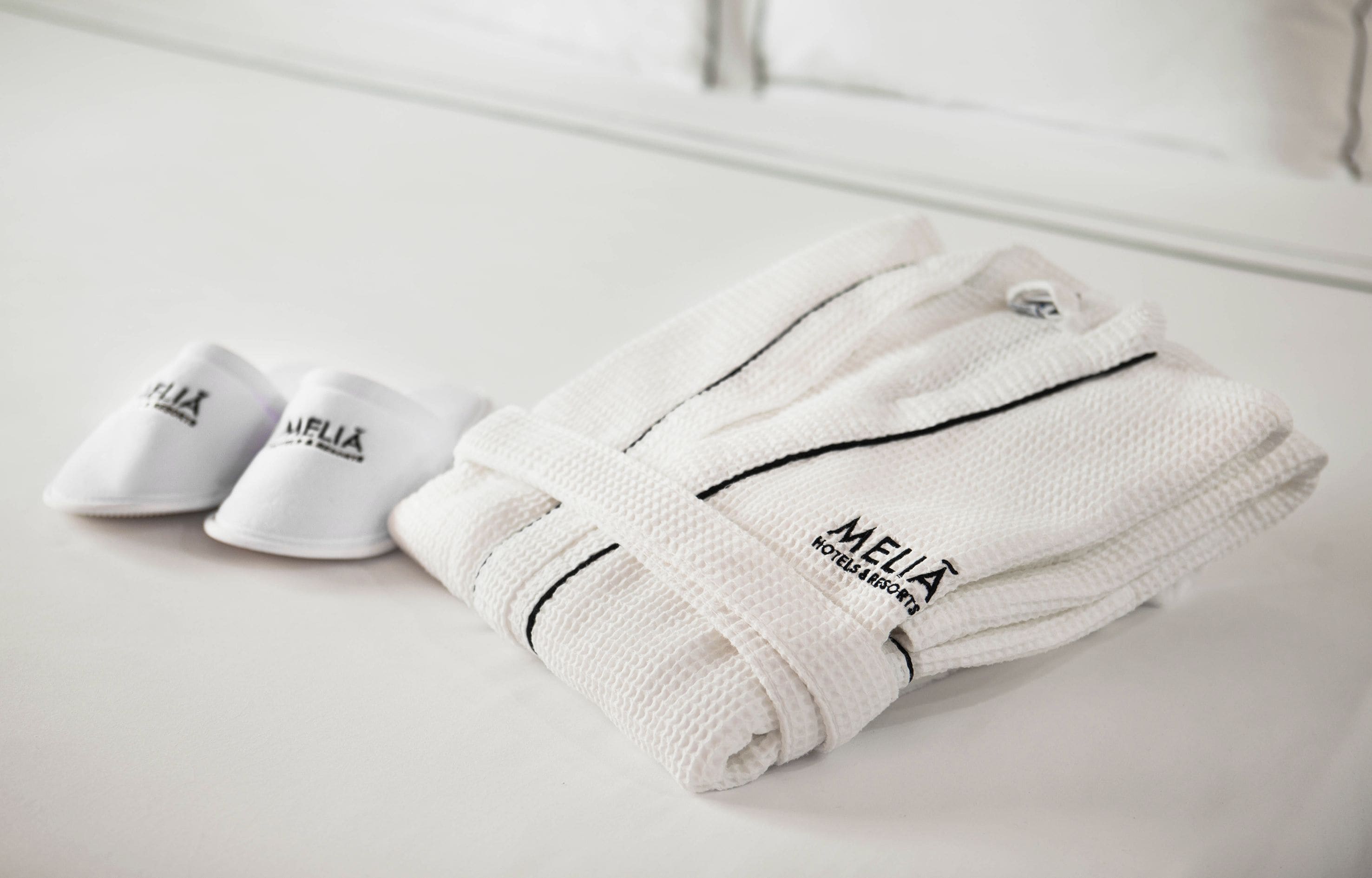 A neatly folded white towel and slippers with the brand 'MELIA' visible, placed on a white surface.