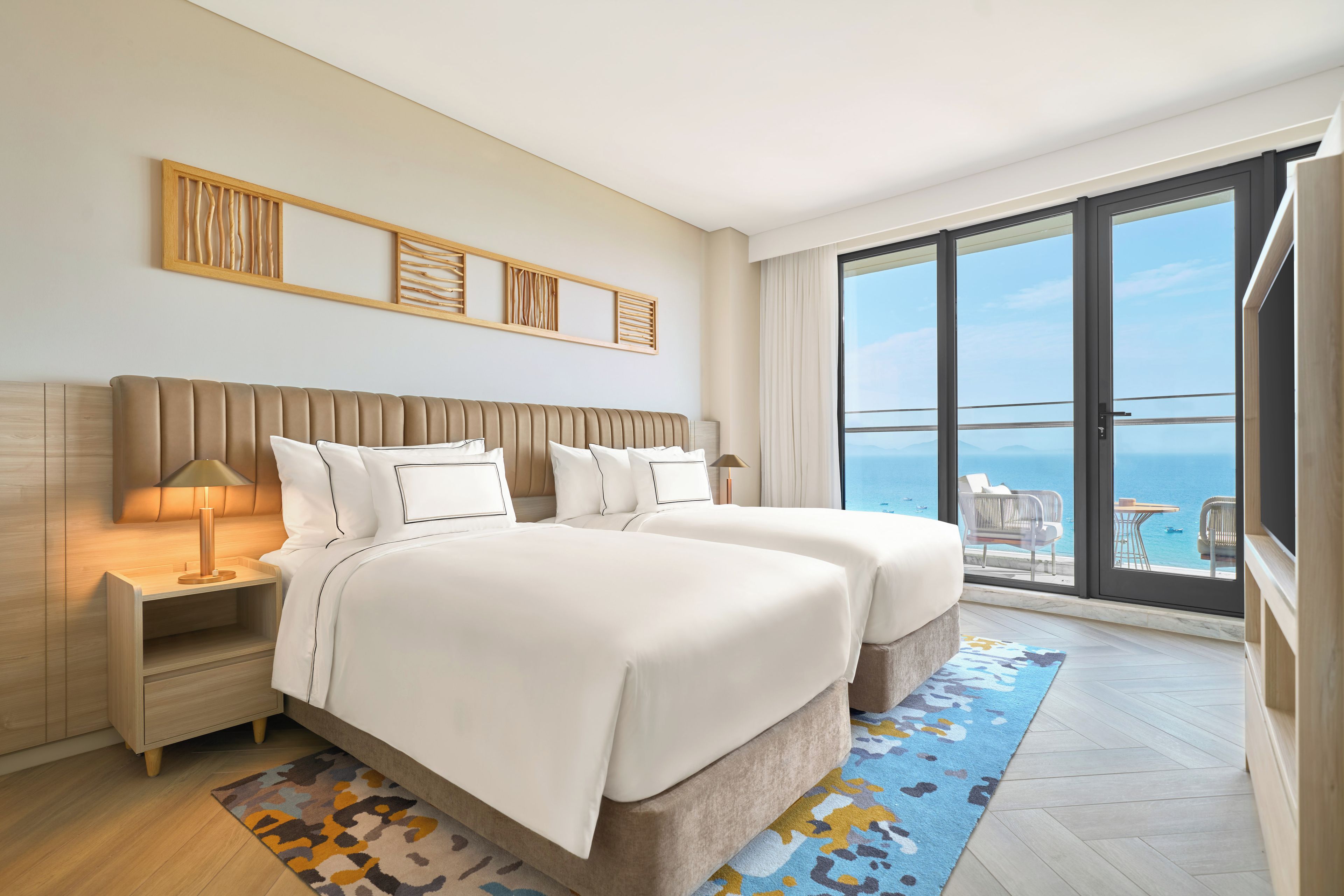 A hotel room with a large balcony, a bed with white linens, and a view of the sea.