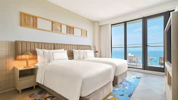 A hotel room with a large balcony, a bed with white linens, and a view of the sea.