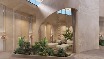 Un hall d’entrée spacieux, doté d’un plafond haut, de portes en arc de cercle et d’un espace salon central entouré d’une végétation luxuriante.